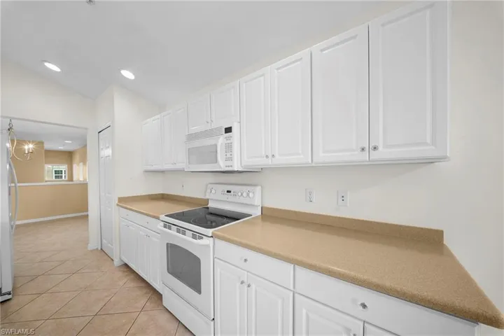 Bright kitchen featuring white cabinetry, a built-in microwave, an electric range, tan countertops, and tiled flooring