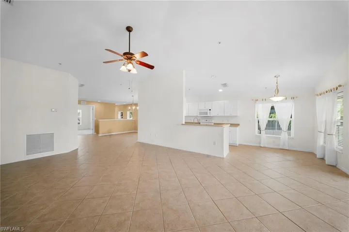 Expansive open-concept living area featuring neutral tile flooring, a ceiling fan with integrated lighting, and a kitchen area with white cabinetry and a built-in microwave