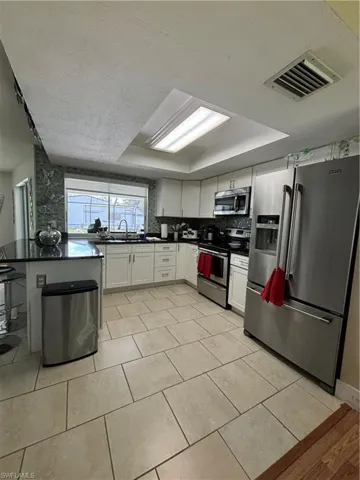 Kitchen featuring refrigerator, dark countertops, range, a tray ceiling, and white cabinets