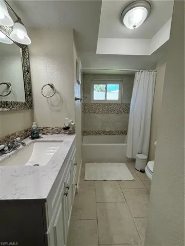 Bathroom with a textured wall, vanity, shower / bath combo, tile patterned flooring, and a textured ceiling