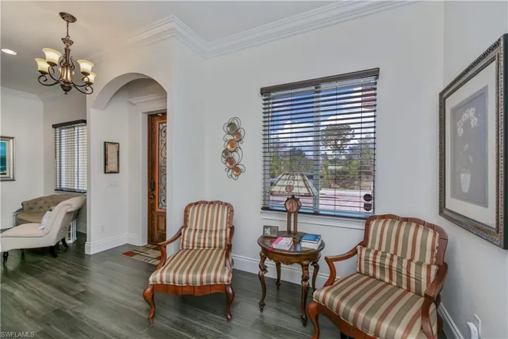 Living area with dark wood-type flooring, ornamental molding, and a notable chandelier
