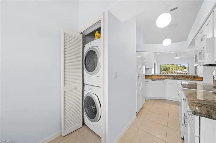 Laundry area featuring stacked washing machine and dryer, light tile patterned floors, and lofted ceiling