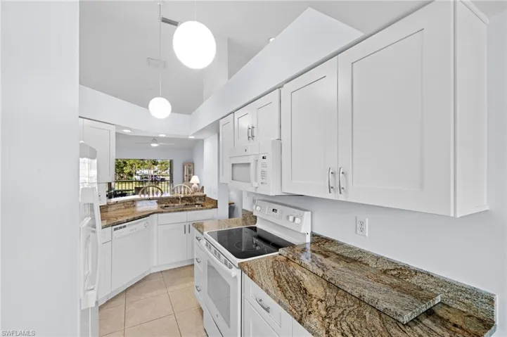 Kitchen with white appliances, dark stone countertops, white cabinetry, light tile patterned flooring, and decorative light fixtures