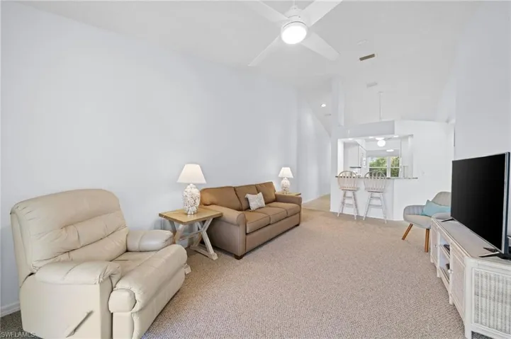 Living area featuring light colored carpet, a ceiling fan, and vaulted ceiling