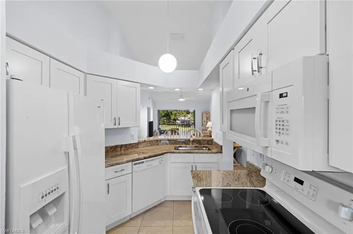 Kitchen featuring white appliances, dark stone counters, white cabinetry, light tile patterned floors, and pendant lighting