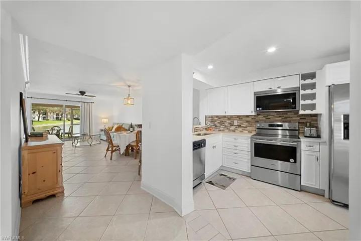 Kitchen featuring stainless steel appliances, white cabinetry, light tile patterned floors, backsplash, and open floor plan