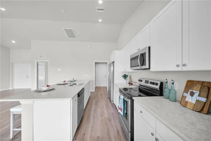 Kitchen with a breakfast bar area, appliances with stainless steel finishes, light wood-style floors, white cabinets, and a sink