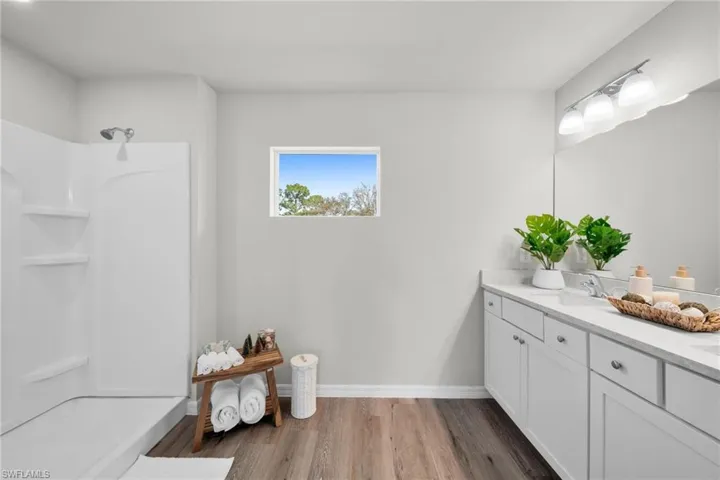 Bathroom featuring baseboards, walk in shower, wood finished floors, and vanity