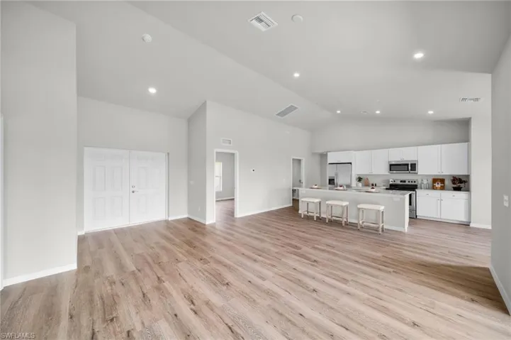Unfurnished living room featuring light wood-style flooring, baseboards, visible vents, and high vaulted ceiling
