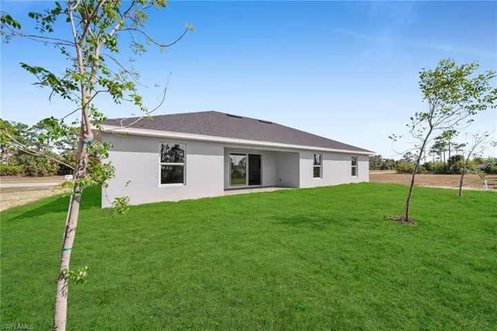 Rear view of property with a lawn, roof with shingles, and stucco siding