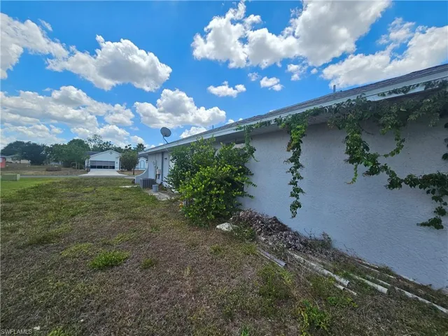 View of side of property featuring cooling unit, stucco siding, and a yard