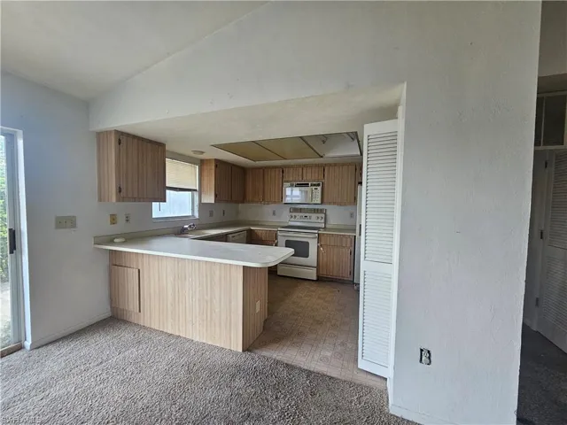 Kitchen featuring white appliances, a peninsula, lofted ceiling, light countertops, and a sink