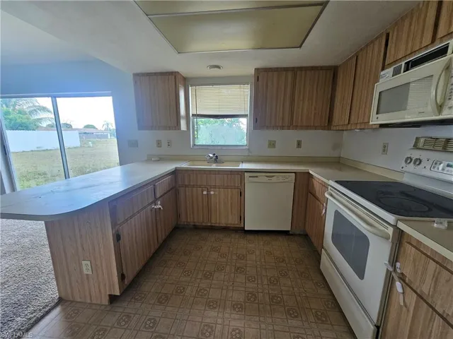 Kitchen featuring white appliances, light countertops, a peninsula, and a sink