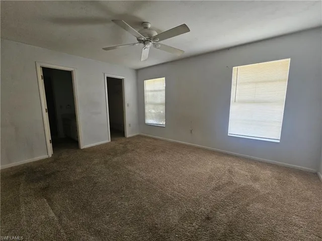 Unfurnished bedroom featuring carpet flooring, baseboards, connected bathroom, and a ceiling fan
