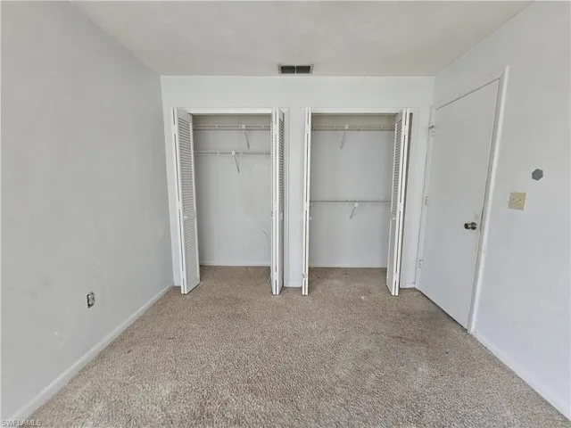 Unfurnished bedroom with carpet floors, two closets, and baseboards