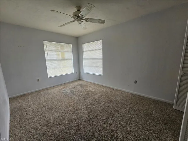 Carpeted spare room featuring ceiling fan and baseboards