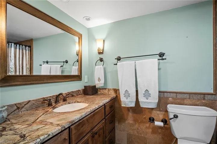 Bathroom featuring a wainscoted wall, vanity, tile walls, and toilet