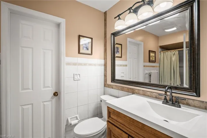 Full bath with tile walls, toilet, vanity, and a wainscoted wall