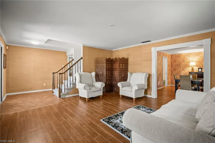 Living room with stairs, wallpapered walls, wood finished floors, and ornamental molding