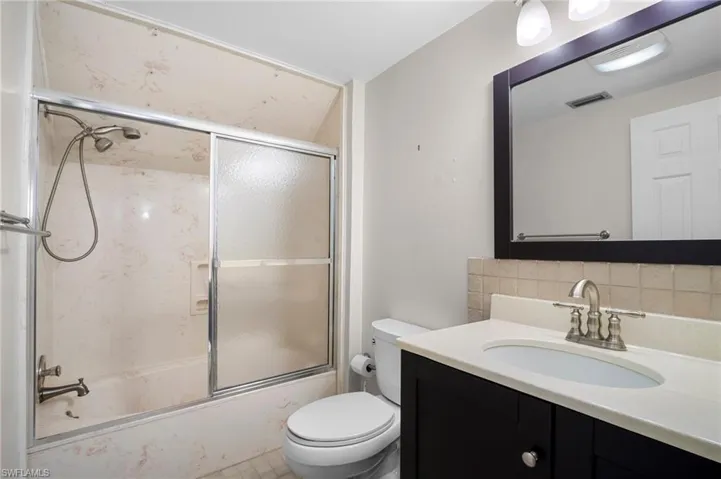 Bathroom featuring vanity, toilet, tasteful backsplash, and combined bath / shower with glass door