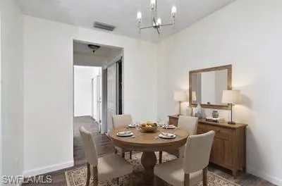 Dining area featuring wood-finish flooring, white wall finishes, and a contemporary chandelier