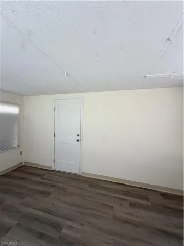 Spacious room with wood-finish flooring, light-colored walls, and a white paneled door