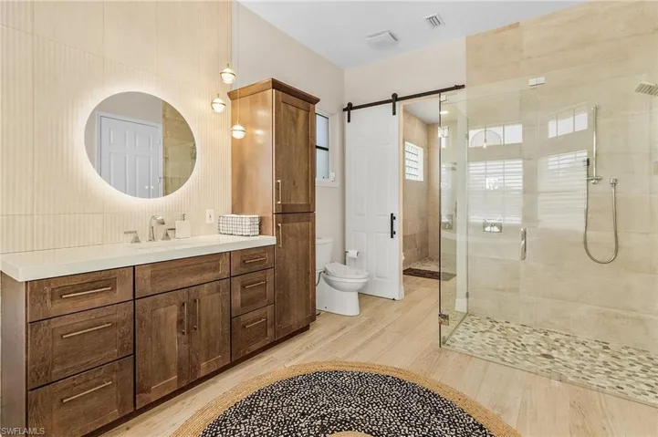 Bathroom featuring a shower stall, vanity, wood finished floors, tile walls, and decorative backsplash