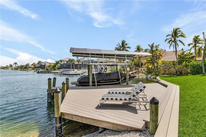 Dock area with a water view, boat lift, and a lawn