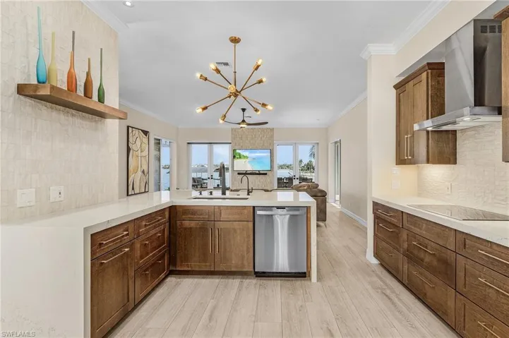 Kitchen with stainless steel dishwasher, wall chimney exhaust hood, open shelves, a chandelier, and a peninsula