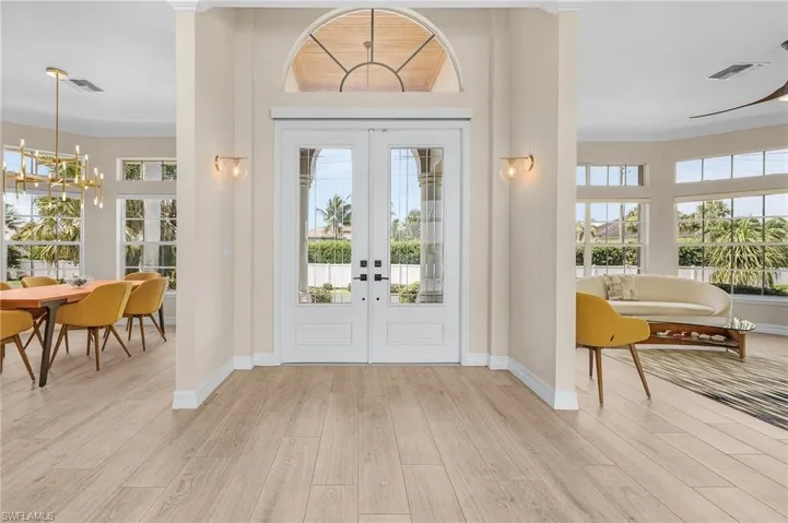 Entrance foyer with french doors, a chandelier, light wood-style floors, and crown molding