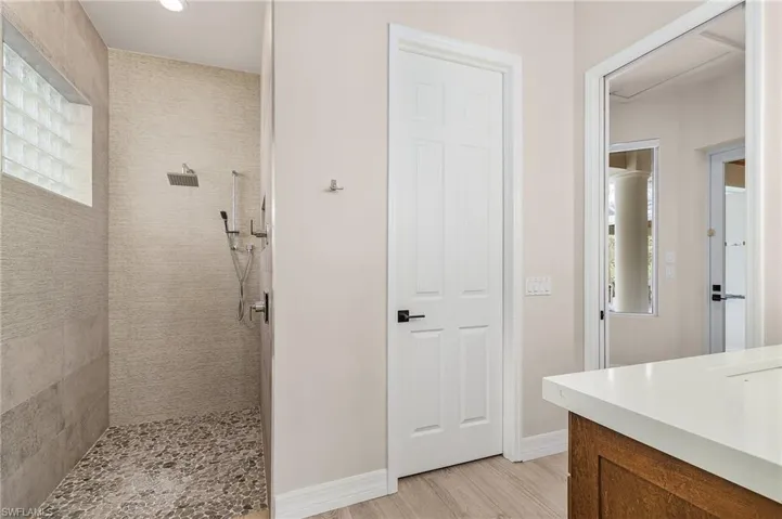 Bathroom featuring a tile shower, vanity, wood finished floors, and recessed lighting