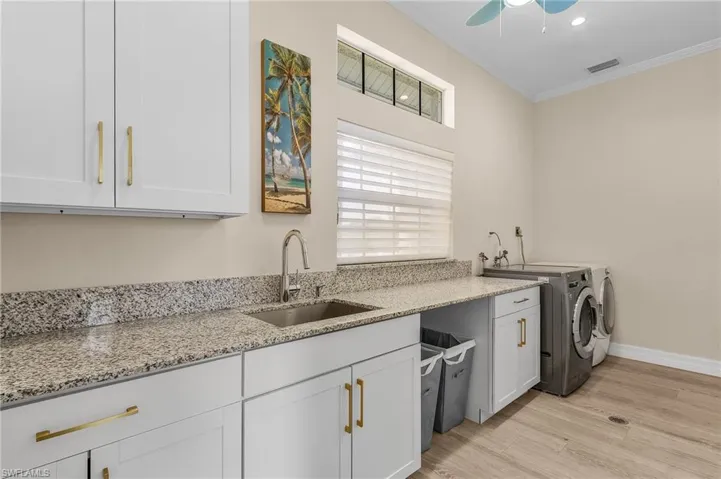 Kitchen featuring washing machine and clothes dryer, light wood-style floors, ornamental molding, a ceiling fan, and light stone counters