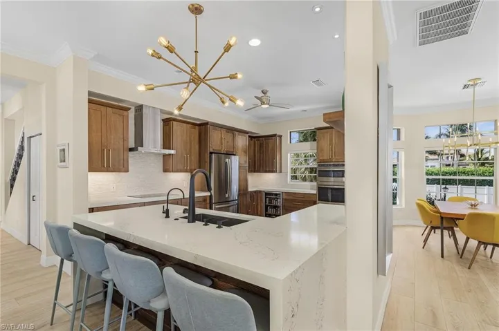 Kitchen featuring a chandelier, wall chimney range hood, stainless steel appliances, crown molding, and decorative backsplash