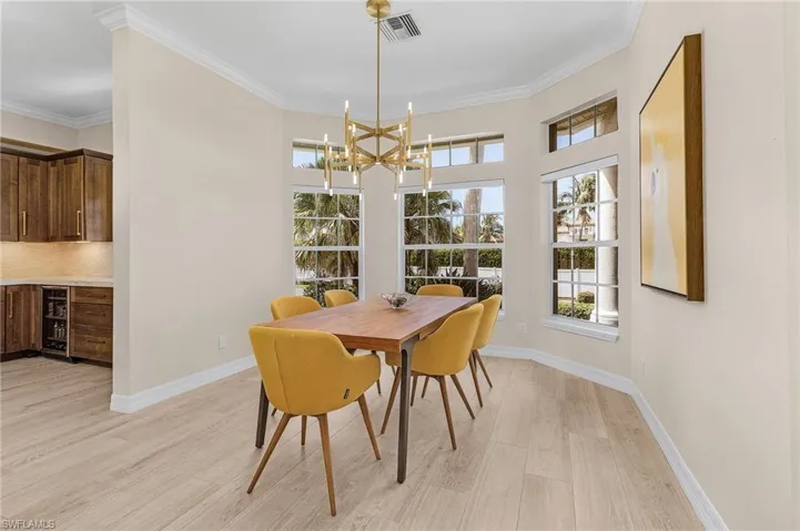 Dining space featuring light wood-type flooring, a chandelier, wine cooler, and crown molding