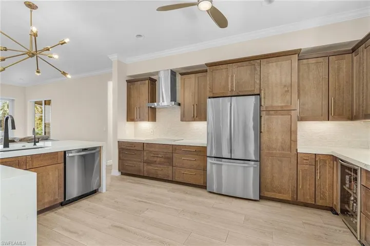 Kitchen featuring appliances with stainless steel finishes, wall chimney range hood, ornamental molding, backsplash, and ceiling fan