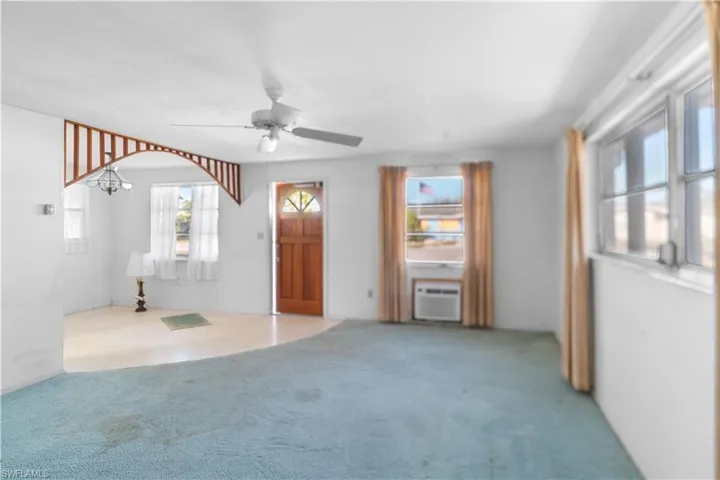 Unfurnished living room featuring light carpet, ceiling fan with notable chandelier, and a wall unit AC