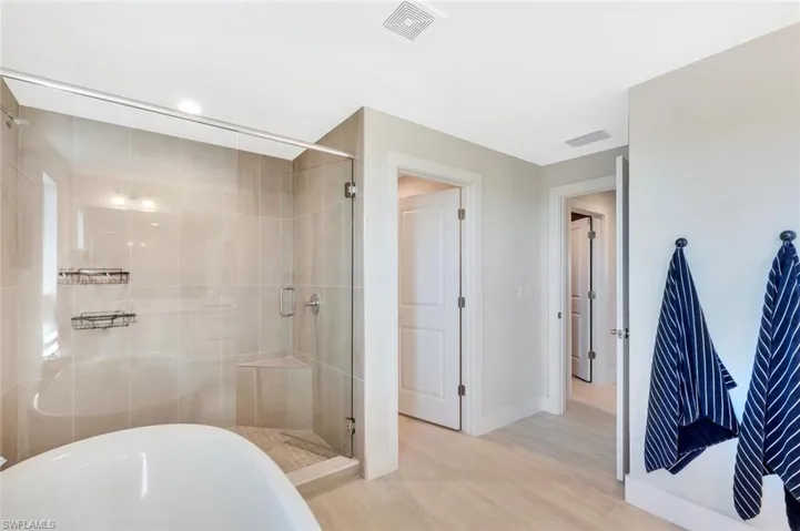 The primary bathroom at Preservation is a serene, spa-inspired retreat designed for both relaxation and refined daily living. A freestanding soaking tub anchors the space, creating a sculptural focal point that pairs beautifully with the expansive walk-in shower wrapped in floor-to-ceiling tile. The frameless glass enclosure and subtle neutral palette enhance the natural light, giving the room an airy, calming feel.Clean lines and warm textures carry through to the double entry doors and light wood-look