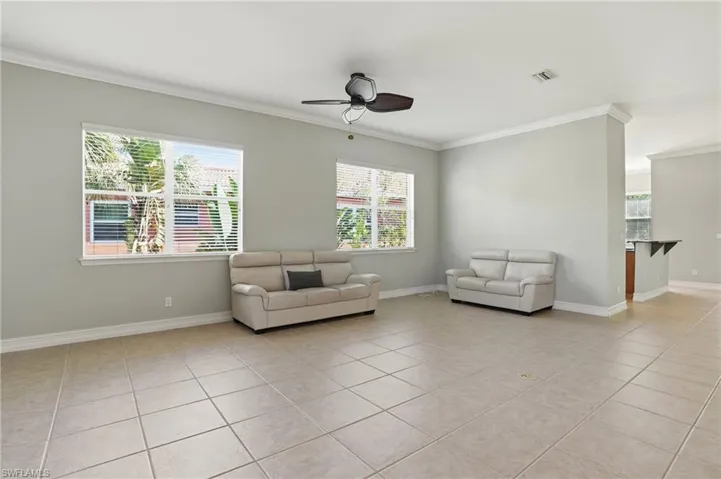 Living room with a ceiling fan, ornamental molding, and light tile patterned flooring