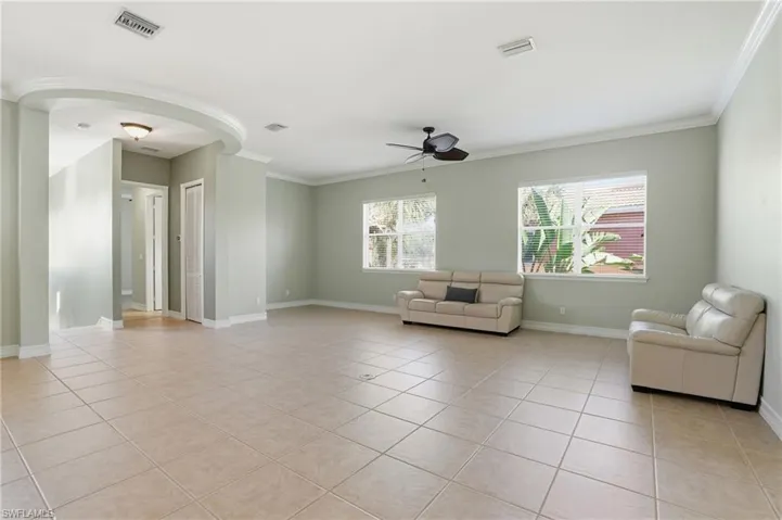 Living area with a ceiling fan, arched walkways, light tile patterned flooring, and ornamental molding