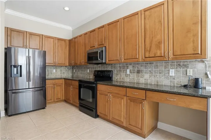 Kitchen with wood finish cabinets, stainless steel appliances, dark stone counters, ornamental molding, and decorative backsplash
