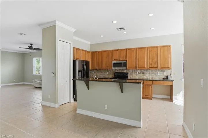 Kitchen with a kitchen bar, dark stone counters, crown molding, an island with sink, and stainless steel appliances