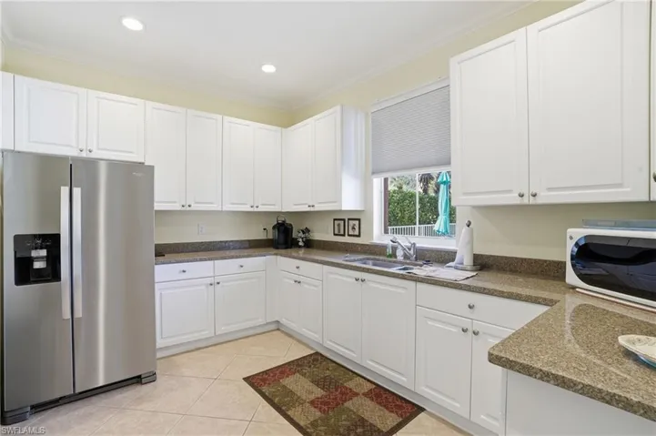Kitchen featuring stainless steel fridge, white cabinetry, dark stone countertops, white microwave, and crown molding