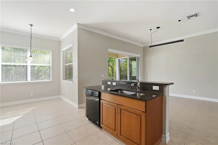Kitchen with hanging light fixtures, wood finish cabinetry, dark stone counters, a kitchen island with sink, and crown molding