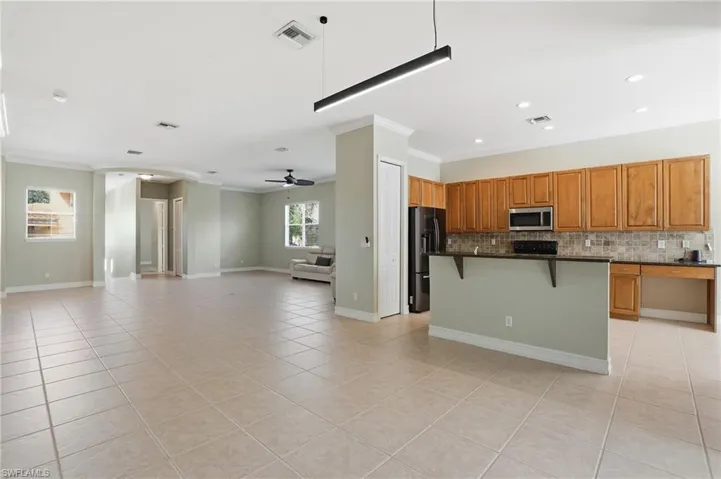 Kitchen featuring a breakfast bar, wood finish cabinetry, ornamental molding, a kitchen island, and black fridge with ice dispenser