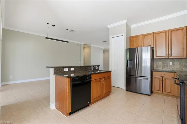 Kitchen featuring black appliances, wood finish cabinets, ornamental molding, light tile patterned floors, and a kitchen island with sink