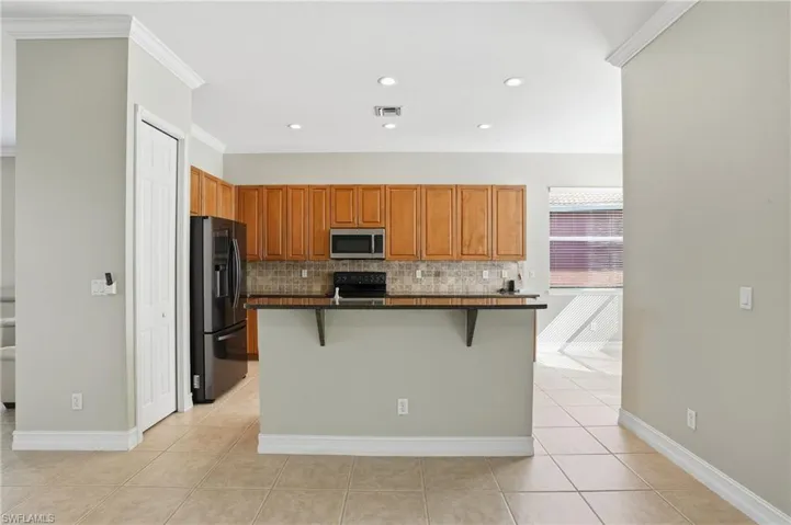 Kitchen with a breakfast bar, black appliances, wood finish cabinetry, an island with sink, and tasteful backsplash