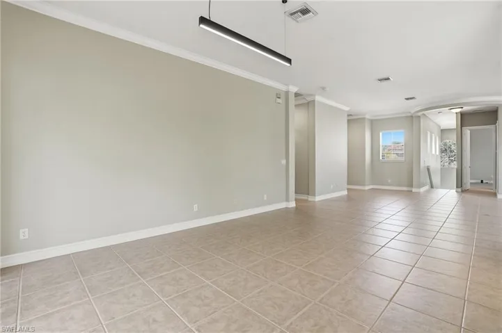Empty room with crown molding, light tile patterned floors, and ornate columns