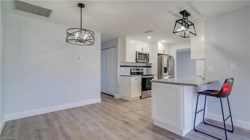 Kitchen featuring white cabinetry, dark hardwood / wood-style flooring, stainless steel appliances, light stone counters, and tasteful backsplash