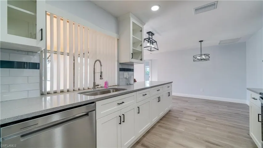 Kitchen featuring light stone counters, light hardwood / wood-style flooring, stainless steel appliances, tasteful backsplash, and white cabinets