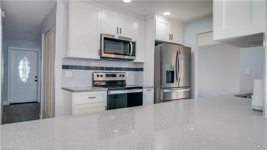 Kitchen featuring light hardwood / wood-style flooring, hanging light fixtures, tasteful backsplash, stainless steel dishwasher, and white cabinets